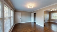 Located in Louisville's 40204 neighborhood, this single-floor home at 2315 Glenmary Ave offers a well-considered layout with consistent, appealing finishes throughout. Rich, dark hardwood flooring runs seamlessly across the living areas and bedrooms, anchoring each room with warmth and character. Neutral taupe and gray wall tones complement the white trim and crown molding found in several rooms, lending a clean, cohesive aesthetic. Multiple bedrooms feature natural light through white-framed windows with blinds, and several include closet storage. The main living and dining areas are accented by crown molding and contemporary light fixtures, adding a refined touch to the open, airy feel. The bathroom retains a classic charm with a black-and-white mosaic tile floor, white subway tile surround, a soaking tub, and oil-rubbed bronze fixtures, topped by a window that brings in natural light. The kitchen and laundry area is well-appointed with granite countertops, white cabinetry, a subway tile backsplash, a matte black faucet, stainless steel sink, and a stacked washer and dryer unit — all set on a bold black-and-white checkered floor. Built-in shelving near the bathroom adds practical storage. The overall ambiance is tidy, move-in ready, and thoughtfully updated.