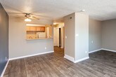 This single-floor space offers a practical and comfortable layout designed to make efficient use of every room. The living area is a standout, featuring rich dark wood-look flooring, neutral taupe walls, and a bold navy blue accent wall that adds a modern touch. A large window fitted with vertical blinds allows natural light to fill the room, creating a bright and welcoming atmosphere. The textured ceiling adds classic character throughout the living spaces.

The kitchen is well-appointed with warm honey-toned wood cabinetry providing ample upper and lower storage. Light laminate countertops offer generous prep space, complemented by a double stainless steel sink, a dishwasher, and an electric range, making it a fully functional cooking area. Light wood-look flooring ties the kitchen seamlessly to the rest of the unit.

A second room features the same neutral tones and dark wood-look flooring, offering a versatile space suitable for a bedroom or additional living area, with its own textured ceiling and clean, simple finishes.

The bathroom is clean and well-maintained, featuring a full-size soaking tub with a tiled shower surround, chrome fixtures, and a shower curtain rod. The wood-look flooring continues here, maintaining a cohesive design throughout the entire space.