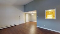 This single-floor, 2-bedroom, 1-bathroom residence offers a well-organized and efficient layout designed to maximize comfort and functionality. The living area immediately impresses with its dramatically vaulted ceilings, which lend a sense of openness and volume well beyond the footprint of the space. Rich, dark hardwood flooring runs throughout, providing warmth and a cohesive aesthetic that ties the rooms together seamlessly.

The main living area flows naturally into a dedicated dining space, distinguished by a classic chandelier that adds a touch of elegance to everyday gatherings. Soft, neutral tones on the walls — including a muted blue-grey accent — create a calm and inviting atmosphere throughout. White trim and baseboards provide clean contrast, enhancing the overall brightness of the interior.

A baseboard heating system is visible along the perimeter, ensuring year-round comfort. The entryway is practical and well-defined, featuring a solid white front door alongside a secondary interior door, offering convenient access and storage options.

With two bedrooms and a full bathroom, this home strikes a practical balance between shared living spaces and private quarters, making it a comfortable and functional choice for a variety of lifestyles.