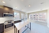 Located at 21 Charles St in Cambridge, MA, this well-designed 2-bedroom, 2-bathroom residence offers a thoughtfully efficient single-floor layout. The open-concept kitchen and living area serves as the heart of the home, bathed in natural light through multiple large windows that frame urban Cambridge views. The kitchen is appointed with dark wood cabinetry, white quartz countertops, a subway tile backsplash, and a full suite of stainless steel appliances including a gas range, built-in microwave, and French door refrigerator. A central island provides additional prep and dining space. Light wood-tone flooring runs throughout, lending a clean, cohesive aesthetic. The two bedrooms are comfortably sized, each with large windows offering city views and ample closet space—three closets total are distributed throughout the unit. The bathrooms are finished with white subway tile walls and dark floor tile; one features a glass-enclosed walk-in shower, while the other includes a soaking tub. A dedicated laundry area and a connecting hallway complete the layout. Recessed lighting and neutral warm-toned walls throughout contribute to a bright, modern ambiance.