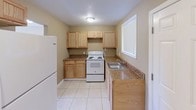 This single-floor apartment at Sanford Estates Apartments offers a practical and straightforward layout across several distinct spaces. The living area features light-toned ceramic tile flooring, warm beige walls, and a large window fitted with vertical blinds that allow natural light to fill the room. A wall-mounted air conditioning unit provides climate control, and flush-mount ceiling fixtures provide overhead lighting throughout the tiled areas.

The kitchen is equipped with light oak cabinetry, granite-patterned countertops, a white electric range, a full-size Whirlpool refrigerator, and a stainless steel sink positioned beneath a window. The tile flooring continues throughout the kitchen, complementing the functional and organized layout.

Multiple bedrooms feature dark, plush carpeting, warm beige walls, white baseboards, and individual windows with vertical blinds that provide natural light and outdoor views. Textured ceilings are present in several rooms, adding a consistent design element throughout.

The bathroom includes tile flooring, a tiled tub-shower surround, a white vanity with under-sink storage, and a window with vertical blinds. A dedicated laundry area with upper cabinetry, washer and dryer hookups, and additional storage rounds out the unit's practical offerings.