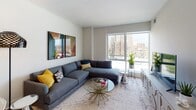 Located on the 8th floor at 710 12th St in Arlington, Virginia, this well-appointed unit offers a thoughtfully designed single-floor layout with modern finishes and sweeping city views. The entry foyer features a rich wood-toned door with a sleek lever handle, setting a contemporary tone from the moment you arrive. Light hardwood flooring runs through the main living areas, complementing the clean, neutral palette throughout.

The open kitchen is a standout feature, showcasing two-tone cabinetry — dark walnut lowers paired with crisp white uppers — alongside stainless steel appliances, a tile backsplash, and a generous island with pendant lighting and bar seating. The kitchen flows seamlessly into the dining and living areas, making it ideal for entertaining.

The living room is bathed in natural light from floor-to-ceiling windows that frame expansive views of the Arlington skyline. A large sectional sofa and bold abstract artwork add character to the bright, airy space.

The bedroom continues the theme of comfort and style, featuring large windows with city views, soft neutral tones, a statement brass chandelier, and warm mid-century modern furnishings. The bathroom offers a clean, contemporary design with navy cabinetry and light tile flooring. Every detail of this space reflects a cohesive, modern aesthetic.