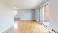 This 2-bedroom, 1-bathroom unit offers a functional and well-organized single-floor layout. Warm parquet wood flooring runs throughout the main living areas and bedrooms, lending a classic character to the interior. The combined kitchen and living room area forms the heart of the unit. The living room is generously proportioned, bathed in natural light through large sliding glass doors that open to an outdoor view, and is equipped with baseboard heating. The galley-style kitchen features ample white cabinetry on both sides, a full suite of white appliances including an electric range and refrigerator, a single-basin sink, and light tile flooring — a clean and practical space for cooking.

The primary bedroom is a comfortable size, featuring parquet flooring, a window overlooking the surrounding brick exterior, a built-in closet, and baseboard heating. The second bedroom mirrors this layout with its own closet, parquet floors, and natural light. Both rooms are finished in neutral tones. The entrance foyer provides a clear transition into the unit with tile flooring. The bathroom includes a full bathtub with white tile surround and a chrome grab bar. Overall, the unit presents a clean, neutral palette throughout, making it a practical and versatile living space.