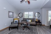 This single-floor residence offers a thoughtfully designed layout that balances comfort and functionality across its key living spaces. The living room features wood-look flooring, a ceiling fan, and natural light from a large window, creating a warm and inviting atmosphere. An open passage connects seamlessly to the dining area, which is brightened by additional windows draped with floral-accented curtains and anchored by a pendant light overhead. The galley-style kitchen runs parallel to the dining space and is equipped with ample white cabinetry, a double sink, and stainless steel appliances including a refrigerator, microwave, and range. The primary bedroom is a restful retreat with plush carpet, a ceiling fan, and direct access to both a walk-in closet and a private en-suite bathroom. Two additional bedrooms offer ceiling fans and closet storage, providing flexible space for guests or home office use. Two full bathrooms serve the home, each featuring a tub-shower combination. Neutral gray tones and wood-look flooring throughout the common areas lend a cohesive, modern aesthetic, while carpeted bedrooms add warmth and comfort to the private spaces.