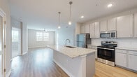 This single-floor residence showcases a contemporary open-concept design that seamlessly connects the kitchen and living areas. The kitchen is a standout feature, centered around a large island with a granite countertop and an undermount sink, illuminated by sleek pendant lights. Gray cabinetry lines the walls alongside a full suite of stainless steel appliances, including a refrigerator, range, microwave, and dishwasher. A white tile backsplash and wood-style flooring complete the kitchen's clean, modern aesthetic.

The living area extends naturally from the kitchen, offering generous open space bathed in natural light from multiple windows fitted with horizontal blinds. A ceiling fan anchors the room, contributing to the bright, airy ambiance.

The bedrooms are carpeted and well-proportioned, each featuring ceiling fans and windows that allow ample natural light. The primary bathroom includes a double-sink vanity with granite countertops, a glass-enclosed shower, and wood-style flooring, while the secondary bathroom offers a tiled tub-shower combination with matching granite finishes. Throughout, neutral tones and consistent finishes create a cohesive, move-in-ready environment.