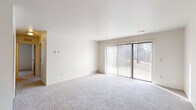 This single-floor residence offers a clean, functional layout designed for comfortable everyday living. The generously sized living area is finished with plush light-gray carpeting and crisp white walls, creating a bright and open atmosphere. A large sliding glass door fitted with vertical blinds fills the space with natural light while providing views of the surrounding greenery and direct access to the outdoors. A hallway connects the living area to the private quarters of the home.

The bedrooms are carpeted and well-proportioned, each featuring windows with vertical blinds that allow for natural light and outdoor views. One bedroom offers dual closets with warm wood-toned panel doors, providing ample storage. The full bathroom includes a tub-shower combination with white tile surround, a vanity with storage, and tile flooring in a warm earth tone.

The kitchen is equipped with a range, refrigerator, and cabinetry, offering a practical workspace. A dedicated utility area houses a full-size washer and dryer alongside a water heater, adding in-unit convenience. Throughout the space, the neutral color palette, consistent carpeting, and straightforward design create a cohesive and move-in-ready environment.