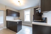 Located on Maitland Street in Toronto's vibrant Church-Wellesley neighbourhood, this two-bedroom, one-bathroom unit thoughtfully combines historic character with contemporary finishes across a single floor. The living room serves as a standout feature, showcasing gleaming hardwood floors, a decorative bay window framing natural light, and a classic fireplace with an ornate cast-iron insert flanked by elegant white-trimmed windows — one of which features a decorative leaded glass transom. The kitchen is outfitted with dark wood cabinetry, white countertops, stainless steel appliances including a refrigerator and electric range, and light tile flooring, accessed through a classically trimmed doorway. Both bedrooms continue the warm hardwood flooring and are equipped with traditional cast-iron radiators, with one bedroom offering a bright street-facing window. The bathroom features a glass-enclosed shower stall with white subway tile, mosaic tile flooring, and a contrasting decorative tile accent border. A connecting hallway with original architectural trim ties the layout together, preserving the building's heritage character throughout.
