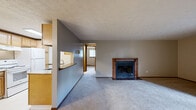 Located at 1880 Beechwood in North Canton, Ohio, this two-bedroom, one-bathroom residence offers a practical and comfortable single-floor layout. The combined living room and kitchen area forms the heart of the home, where a wood-trimmed fireplace with tile surround serves as a focal point in the carpeted living room. A sliding glass door brings in natural light and provides outdoor access, complemented by a textured ceiling and baseboard heating throughout. The galley-style kitchen features warm oak cabinetry, granite-look countertops, white appliances including a range and refrigerator, and a skylight that brightens the space with natural overhead light. Tile flooring and a dedicated dining area with a ceiling fan round out the kitchen zone. The primary bedroom is generously sized and includes large sliding wood-panel closet doors and a ceiling fan with a window for natural light. The second bedroom is comfortably scaled with its own closet and baseboard heating. The full bathroom is finished with tile flooring, a wood-toned vanity with white countertop, and a shower-tub combination. A connecting hallway ties the rooms together, creating an efficient and well-organized floor plan throughout the home.