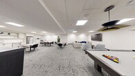 Located at 1475 Whites Rd in Pickering, Ontario, this well-appointed amenity space offers a thoughtfully designed single-floor layout that seamlessly blends recreation, dining, and relaxation. The interior is finished in a clean, contemporary style, with crisp white walls, a suspended grid ceiling with recessed LED panel lighting, and a striking geometric-patterned grey carpet that flows throughout the space.

The lounge area anchors one end of the room, featuring a large sectional sofa, rounded accent chairs, a low circular coffee table, and a wall-mounted flat-screen television. Abstract blue-and-white artwork decorates the walls, adding a sophisticated visual touch. Adjacent to the lounge is a games area equipped with a pool table and cue rack, along with bar-height seating and a classic arcade cabinet, making it an engaging space for recreation.

A casual dining and gathering zone occupies the central area, with multiple round and rectangular tables surrounded by modern chairs. This transitions naturally into a fully equipped kitchenette featuring white cabinetry, stainless steel appliances including a refrigerator and oven, open shelving with decorative accents, and tile flooring. A wall-mounted television and open shelving unit complete the functional yet stylish breakroom feel. The overall ambiance is modern, bright, and welcoming.