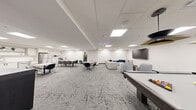 Located at 1475 Whites Rd in Pickering, Ontario, this well-appointed amenity space offers a thoughtfully designed single-floor layout that seamlessly blends recreation, dining, and relaxation. The interior is finished in a clean, contemporary style, with crisp white walls, a suspended grid ceiling with recessed LED panel lighting, and a striking geometric-patterned grey carpet that flows throughout the space.

The lounge area anchors one end of the room, featuring a large sectional sofa, rounded accent chairs, a low circular coffee table, and a wall-mounted flat-screen television. Abstract blue-and-white artwork decorates the walls, adding a sophisticated visual touch. Adjacent to the lounge is a games area equipped with a pool table and cue rack, along with bar-height seating and a classic arcade cabinet, making it an engaging space for recreation.

A casual dining and gathering zone occupies the central area, with multiple round and rectangular tables surrounded by modern chairs. This transitions naturally into a fully equipped kitchenette featuring white cabinetry, stainless steel appliances including a refrigerator and oven, open shelving with decorative accents, and tile flooring. A wall-mounted television and open shelving unit complete the functional yet stylish breakroom feel. The overall ambiance is modern, bright, and welcoming.