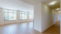 This single-floor residence is designed with a clean, contemporary aesthetic that emphasizes natural light and open space throughout. The expansive living area features light-toned hardwood flooring and a wall of large windows fitted with horizontal blinds, allowing abundant natural light to fill the room. A glass door provides direct access to an outdoor balcony, enhancing the sense of openness. The kitchen is outfitted with sleek white cabinetry extending to the ceiling, stainless steel appliances including a gas range, over-the-range microwave, dishwasher, and a side-by-side refrigerator with an ice and water dispenser, all set atop the same warm hardwood floors. The bedrooms are generously sized, each with hardwood flooring and windows offering outdoor views. The primary bathroom features a dual-sink vanity with granite countertops, white cabinetry, a glass-enclosed walk-in shower with tile surround, and tile flooring. Additional bathrooms mirror this refined finish, offering granite countertop vanities, tile surrounds, and combination tub-shower units. The overall design is cohesive and neutral, creating a bright, inviting atmosphere throughout the residence.