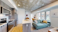 This modern 2-bedroom, 2-bathroom unit at 30 Rue Jos-Montferrand in Gatineau, QC offers a thoughtfully designed open-concept layout on a single floor. A defining architectural feature throughout the main living area is the exposed concrete ceiling, lending an industrial-chic character balanced by crisp white walls and warm light wood flooring.

The kitchen is well-appointed with wood-grain cabinetry extending to the ceiling, a full suite of stainless steel appliances including a French-door refrigerator, electric range, microwave, and dishwasher, along with a light-toned countertop island that flows seamlessly into the living and dining areas. Large floor-to-ceiling windows flood the dining and living spaces with natural light while offering urban views of the surrounding cityscape.

The two bedrooms are comfortably proportioned, with the primary featuring the signature exposed concrete ceiling detail and light wood flooring. Both bathrooms are finished with clean, contemporary fixtures — one featuring a glass-enclosed shower and wood-grain vanity, and the other with a full soaking tub framed by large-format grey tile. The overall ambiance is modern, bright, and cohesive, making efficient and stylish use of the available space.