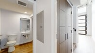 Located at 3279 San Marino St, Unit 405, in Los Angeles, this two-story loft offers a thoughtfully designed layout spread across two levels. The main floor features an open-concept living and kitchen area with soaring ceilings that amplify the sense of space. The kitchen is outfitted with modern flat-front cabinetry in a warm wood tone, stainless steel appliances including a refrigerator, gas range, and built-in microwave, and a clean white countertop. Light wood-tone flooring runs throughout, lending warmth and continuity to the space. A striking wall of floor-to-ceiling industrial-style windows with black framing floods the main living area with natural light and opens to a balcony with city views — a true standout feature. The upper loft level, accessed via an interior staircase, provides a more intimate retreat with a wall-mounted mini-split system for climate control. The bathroom is well-appointed with a walk-in glass shower, a wall-mounted sink, a sleek black-framed mirror, and the added convenience of an in-unit washer. The angled ceiling detail in the bathroom reflects the architectural character of the loft layout. Clean white walls throughout contribute to a bright, contemporary ambiance ideal for urban living in the heart of Los Angeles.