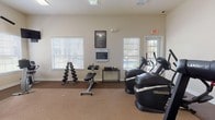 Located at 150 Du Rhu Dr in Mobile, Alabama, this single-floor fitness center is a well-equipped exercise facility designed to support a comprehensive workout routine. The space is organized into distinct workout zones, each catering to different training needs.

The cardio area is a standout feature, housing multiple Landice treadmills and Octane elliptical/stair-style machines, providing ample options for aerobic exercise. Wall-mounted televisions are positioned throughout for entertainment during workouts. The carpeted flooring and neutral-toned walls create a clean, functional environment throughout.

A dedicated strength training section includes a multi-station cable weight machine, ideal for a variety of resistance exercises targeting different muscle groups. A free weight station rounds out the strength area, featuring a rack of dumbbells in graduated sizes alongside an adjustable weight bench, accommodating both beginners and experienced lifters.

Natural light filters in through multiple windows dressed with horizontal blinds, offering views of the surrounding outdoor area, including glimpses of a pool. The space also includes sanitizing stations, posted workout guidelines and fitness center rules, and clearly marked emergency exits, reflecting attention to both safety and cleanliness. Overall, the facility delivers a practical and inviting environment for residents seeking a convenient on-site fitness option.