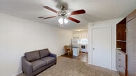 Located at 296 Muellers Circle in Statesville, NC, this single-floor unit offers a practical and efficient layout across its modest footprint. The open-concept living area features neutral carpet flooring, a textured ceiling, and a ceiling fan with integrated lighting, contributing to a comfortable and airy atmosphere. A window with a view of the outdoors allows natural light to filter in, brightening the space. A wall-mounted air conditioning unit provides convenient climate control.

The kitchen flows seamlessly from the living area and is equipped with white cabinetry, a white refrigerator, and a white electric range. A dark-topped kitchen island doubles as a dining surface, accompanied by warm wood-toned chairs, making efficient use of the available space. The transition between the carpeted living area and the kitchen's wood-look hardwood flooring clearly delineates each zone.

The bathroom is clean and simply appointed, featuring wood-look vinyl plank flooring, crisp white walls, a toilet, vanity, and a bathtub with a shower. Chrome towel bars add a functional finishing touch. Throughout the unit, the light color palette and clean finishes create a bright, well-maintained environment suited for straightforward, comfortable living.