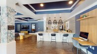 Located at 4209 Lassiter Mill Rd in Raleigh, NC, this single-floor clubhouse is a thoughtfully designed community amenity space that blends bold aesthetics with functional leisure. The interior is defined by a striking navy and white color palette, wood-look tile flooring, and elegantly coffered ceilings with recessed lighting that add depth and architectural interest throughout.

The lounge area offers a comfortable seating arrangement with plush sofas, wicker accent chairs, and a bold geometric area rug in gold and ivory tones. A large flat-screen television is mounted against a deep blue accent wall, complemented by a decorative mirror and curated artwork, creating a warm and inviting retreat.

Adjacent to the lounge, the game room is equipped with a billiards table and a ping-pong table, set beneath coffered ceilings supported by stone-clad columns. Floor-to-ceiling glass walls and sliding doors open directly to an outdoor pool area, filling the space with natural light and seamless indoor-outdoor connectivity.

The kitchenette is finished with white shaker cabinetry, light quartz countertops, a gold-accented faucet, stainless steel appliances, and an eye-catching geometric tile backsplash adorned with abstract artwork. A central bar counter with pendant lighting and bar seating provides an ideal social hub. A dedicated computer workstation area rounds out the amenities of this vibrant community space.