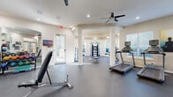 Located at 19017 Portofino Dr in Tampa, FL, this fitness center offers a thoughtfully designed, single-floor workout facility that provides ample space for a full range of exercise activities. The layout is divided into two interconnected zones, seamlessly joined by decorative white columns that add an architectural elegance to the functional space.

The main cardio area features multiple treadmills and stationary bikes, all positioned to take advantage of the natural light streaming through large windows with views of the surrounding greenery. Ceiling fans overhead ensure comfortable airflow throughout workout sessions. Full-length mirrors are strategically placed to maximize the sense of openness and assist with form during exercise.

A dedicated strength training alcove sits within a rounded, bay-style room distinguished by a tray ceiling with recessed lighting and tall arched windows on three sides. This area houses a cable machine, weight bench, resistance equipment, and balance tools such as a stability ball and BOSU trainer, bathed in natural light from all angles.

The entry zone accommodates additional cardio machines, a dumbbell rack, and an adjustable weight bench, all set on durable rubber flooring ideal for high-impact use. Arched doorways frame large mirrors, reinforcing the open, airy atmosphere. Glass entry doors connect the fitness center to the broader facility, completing a cohesive and well-appointed exercise environment.