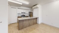 Located at 1795 Rue Berri in the heart of Montréal, this efficiently designed one-bedroom, one-bathroom unit offers a clean, contemporary aesthetic throughout its single floor. Light wood-tone flooring runs continuously across the space, lending warmth and visual cohesion to every room.

The kitchen is a standout feature, equipped with stainless steel appliances including an electric range and a full-size refrigerator, white upper cabinetry, wood-finish lower cabinets, and a peninsula with a quartz-style countertop that doubles as a breakfast bar. A wall-mounted mini-split air conditioning unit provides year-round climate control. The kitchen flows naturally into the combined dining and living area, creating an open, functional layout ideal for everyday living.

The bedroom is a comfortable, well-proportioned room featuring a window with city views and a dedicated closet. Two additional closets—including a larger bi-fold unit in the hallway—provide generous storage rarely found in units of this size. The bathroom is finished with tile flooring, a sliding-door glass shower enclosure, a vanity with wood-tone cabinetry, and a mirrored medicine cabinet. An in-unit laundry area adds everyday convenience. The hallway connects all spaces in a logical flow, completing this well-appointed urban residence.