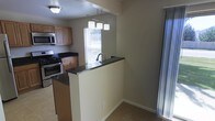 This two-floor home offers a practical and inviting layout designed for comfortable everyday living. The kitchen is a standout feature, equipped with warm wood cabinetry, dark granite-style countertops, and stainless steel appliances including a gas range and over-the-range microwave. A peninsula with a matching dark countertop and an integrated sink extends into the adjacent living area, creating a natural divide between spaces while maintaining an open, connected feel. A pendant light fixture with multiple shades hangs above the peninsula, adding a modern decorative touch and targeted task lighting. Natural light filters into the kitchen through a window fitted with blinds, brightening the space alongside recessed and ceiling-mounted lighting. The flooring transitions from tile in the kitchen to carpet in the living area, subtly defining each zone. Neutral-toned walls throughout contribute to a calm, versatile ambiance that can easily accommodate a variety of interior styles. Sliding glass doors allow additional natural light into the living area and suggest access to an outdoor space. Spanning two floors, this home provides ample room for both living and private quarters, making it a well-rounded and functional residence.