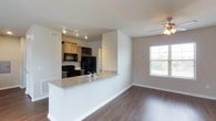 This single-floor residence is designed with an open-concept layout that seamlessly connects the kitchen and living area, creating a spacious and functional environment. The kitchen features warm wood cabinetry, a classic subway tile backsplash, and black appliances, including a refrigerator, range, and microwave. A peninsula with granite countertops and an undermount sink extends into the main living space, providing an ideal area for casual dining or food preparation while maintaining visual connectivity throughout.

The flooring throughout the space is a rich, dark hardwood, adding warmth and contrast to the neutral-toned walls. The living area benefits from a large window that invites natural light and offers a view of the surrounding outdoors, contributing to an open and airy atmosphere. A ceiling fan with a light fixture is installed in the living area, providing both comfort and additional illumination. The overall design balances practicality with modern aesthetics, making the space both inviting and well-suited for everyday living.