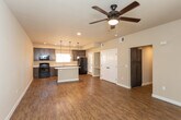 This single-floor residence offers a thoughtfully designed open-concept layout that seamlessly connects the living area and kitchen. The kitchen is a standout feature, showcasing rich dark-stained cabinetry, white countertops, and a full suite of black appliances including a range, microwave, refrigerator, and dishwasher. A central island with a white countertop provides additional workspace and serves as a natural gathering point. Stylish pendant lighting hangs above the island, complementing the recessed lighting throughout. Warm wood-look flooring runs throughout the main living and kitchen areas, lending a cohesive and inviting feel to the space. The open living area is generously proportioned, offering flexibility for a variety of furniture arrangements. The bedrooms feature plush carpeting and are well-lit with natural light from large windows dressed with vertical blinds. One bedroom includes built-in shelving and a walk-in closet, while a ceiling fan adds comfort. The bathrooms are finished with dark cabinetry vanities, white countertops, large mirrors, and tub/shower combinations with clean white surrounds, all accented by the same wood-look flooring found in the main areas. The neutral color palette throughout creates a clean, modern, and move-in-ready atmosphere.