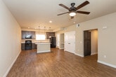 This single-floor residence offers a thoughtfully designed open-concept layout that seamlessly connects the living area and kitchen. The kitchen is a standout feature, showcasing rich dark-stained cabinetry, white countertops, and a full suite of black appliances including a range, microwave, refrigerator, and dishwasher. A central island with a white countertop provides additional workspace and serves as a natural gathering point. Stylish pendant lighting hangs above the island, complementing the recessed lighting throughout. Warm wood-look flooring runs throughout the main living and kitchen areas, lending a cohesive and inviting feel to the space. The open living area is generously proportioned, offering flexibility for a variety of furniture arrangements. The bedrooms feature plush carpeting and are well-lit with natural light from large windows dressed with vertical blinds. One bedroom includes built-in shelving and a walk-in closet, while a ceiling fan adds comfort. The bathrooms are finished with dark cabinetry vanities, white countertops, large mirrors, and tub/shower combinations with clean white surrounds, all accented by the same wood-look flooring found in the main areas. The neutral color palette throughout creates a clean, modern, and move-in-ready atmosphere.