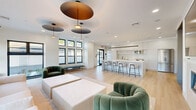 Located at 5 Ledge Dr in Schenectady, NY, this thoughtfully designed single-floor space offers a seamless blend of modern aesthetics and functional living. The open-concept layout connects multiple living areas with a fully equipped kitchen, creating an inviting and versatile environment.

The kitchen is a standout feature, showcasing floor-to-ceiling white shaker cabinetry, stainless steel appliances, a sleek white quartz waterfall island with bar seating, and a linear pendant light overhead. Built-in open shelving adds both storage and visual interest.

The expansive living areas are bathed in natural light from large, black-framed windows that frame outdoor views of the surrounding landscape. A built-in linear gas fireplace serves as a striking focal point, paired with a wall-mounted display above. Sculptural disc pendant lighting and recessed fixtures illuminate the space with warmth and depth.

The entry area makes a memorable first impression with an artistic botanical wallcovering, a sputnik-style chandelier, warm sconce lighting, and a glass-panel automatic door that leads into the main living space.

Light hardwood flooring flows throughout, tying together the crisp white walls and contemporary furnishings. The overall ambiance is clean, sophisticated, and welcoming — ideal for gathering and community engagement.