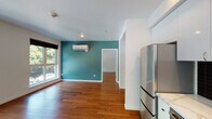 Located in Portland's desirable Northwest neighborhood, this single-floor unit at 2330 NW Raleigh St offers a clean, modern aesthetic throughout. Rich hardwood flooring flows seamlessly across the entire space, complementing the bright white walls and contemporary finishes.

The open-concept living and kitchen area is a standout feature, anchored by large floor-to-ceiling windows that flood the space with natural light and frame views of the surrounding streetscape and mature trees. The kitchen is well-appointed with sleek white cabinetry extending to the ceiling, a bold black tile backsplash, light countertops, and a full suite of stainless steel appliances including a refrigerator, gas range, built-in microwave, and dishwasher.

The living area extends into a secondary room highlighted by a teal accent wall and a wall-mounted mini-split system for efficient climate control. A bedroom features its own large window with neighborhood views, offering a bright and airy retreat. Storage is generously addressed with a spacious walk-in closet equipped with dual hanging rods along three walls.

Two bathrooms serve the space — one with a combined tub and shower, white tile surround, vanity, and large mirror, and a second more compact bathroom with similar clean finishes. The unit's layout is functional and well-organized, reflecting thoughtful modern design throughout.