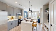 Located at 2220 Wilkinson Boulevard in Charlotte, NC, this thoughtfully designed one-bedroom, one-bathroom residence offers a well-appointed open-concept floor plan across a single level. The combined living, dining, and kitchen area serves as the heart of the home, featuring light wood-style flooring, recessed lighting, and a seamless flow that maximizes the sense of space. The kitchen is outfitted with sleek gray cabinetry, a subway tile backsplash, white quartz countertops, stainless steel appliances including a large French door refrigerator, and a central island with pendant lighting and bar seating. The living area is anchored by a bold blue accent wall and floor-to-ceiling French doors that flood the room with natural light and offer direct views of the Charlotte skyline. The bedroom features a ceiling fan, large windows with city views, and direct access to a walk-in closet. The bathroom includes tile flooring, a tiled soaking tub, and a modern vanity. Additional conveniences include a dedicated laundry area and utility room. Throughout the unit, light-toned walls, wood-look flooring, and contemporary finishes contribute to a bright, cohesive aesthetic with impressive urban views as a backdrop.