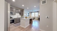 This thoughtfully designed one-bedroom, one-bathroom residence offers an efficient and functional layout across a single floor. The open-concept kitchen and living area serves as the heart of the space, anchored by a central island with granite countertops and bar seating — ideal for casual dining or entertaining. The kitchen is equipped with rich, dark-toned cabinetry, stainless steel appliances including a refrigerator, range, and microwave, and a classic white subway tile backsplash that adds a crisp, contemporary contrast. Light wood-style flooring flows seamlessly throughout, unifying each area of the home. The living room is bright and inviting, benefiting from multiple windows that allow generous natural light and views of the surrounding greenery. A ceiling fan overhead adds both function and style. The bedroom is a comfortable retreat, featuring dual windows, a ceiling fan, and access to a dedicated closet. The bathroom is well-finished with dark cabinetry, granite countertops, a single vanity, and a tiled shower-tub combination. A hallway connects the private sleeping quarters to the main living areas, adding a sense of separation and privacy. Overall, the space presents a clean, modern aesthetic with warm, neutral tones throughout.