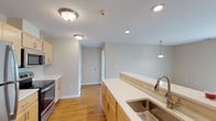 This single-floor residence offers a clean, functional layout designed for comfortable everyday living. The kitchen serves as a central highlight, featuring light maple cabinetry, white countertops, and a full suite of stainless steel appliances including a refrigerator, electric range, and over-the-range microwave. A spacious island with a built-in sink and pendant lighting adds both style and practicality, while warm hardwood flooring ties the space together. Recessed and flush-mount ceiling lights provide ample illumination throughout. The open flow from the kitchen leads toward the living areas, all connected by the same hardwood flooring and neutral wall tones that create a bright, airy atmosphere. The bedrooms are finished with plush carpeting, ceiling fans, and windows dressed with blinds that offer views of the surrounding greenery, along with generous closet space. The bathrooms are consistently appointed with light wood vanities, white countertops, large mirrors with vanity lighting, and glass-enclosed walk-in showers. Stone-look tile flooring in the bathrooms adds a grounded, polished contrast to the softer finishes throughout the rest of the home. Overall, the space presents a cohesive, well-maintained interior with a neutral palette that is both inviting and move-in ready.