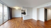 This single-floor residence is designed with a clean, modern aesthetic that balances functional layout with comfortable living spaces. A welcoming entry hallway finished with rich, warm-toned hardwood flooring leads into the main living area, which is bright and open with direct access to a private balcony through expansive floor-to-ceiling sliding glass doors. The generous living space is flooded with natural light and features views of the surrounding outdoors, complemented by dark drapery panels for privacy control.

The galley-style kitchen is well-appointed with gray cabinetry, stone countertops, stainless steel appliances including a refrigerator, range, microwave, and dishwasher, recessed lighting, and a dark tile backsplash. A breakfast bar peninsula connects the kitchen to the living area, offering additional counter space and casual dining options.

The bedrooms are carpeted and feature built-in closets, natural light from windows, and neutral white walls. One bedroom includes a spacious open closet with a rod and shelving system. The bathroom is finished with classic white tile flooring, mosaic tile accents, and a full shower-tub combination with modern fixtures and a grab bar for accessibility.