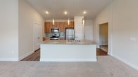 This thoughtfully designed single-floor residence offers a contemporary open-concept layout that seamlessly connects the kitchen and living areas. The kitchen serves as the focal point of the space, showcasing warm wood cabinetry that extends to the ceiling, a light-toned glass tile backsplash, and a full suite of stainless steel appliances including a range, microwave, and refrigerator. A large central island with granite countertops and an undermount sink provides generous workspace and serves as a natural gathering point, illuminated by a trio of elegant pendant lights overhead. Recessed lighting and hardwood-style flooring complete the kitchen's polished look.

The living areas transition to plush carpeting, and the bedrooms feature ceiling fans and neutral tones, offering a calm and comfortable retreat. The primary bathroom is well-appointed with a granite-topped wood vanity, a large frameless mirror, hardwood-style flooring, a glass-enclosed shower, and direct access to a spacious walk-in closet. A private balcony extends the living space outdoors, overlooking a landscaped courtyard framed by the surrounding brick building. The overall aesthetic is clean, modern, and cohesive throughout.