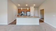 This thoughtfully designed single-floor residence offers a contemporary open-concept layout that seamlessly connects the kitchen and living areas. The kitchen serves as the focal point of the space, showcasing warm wood cabinetry that extends to the ceiling, a light-toned glass tile backsplash, and a full suite of stainless steel appliances including a range, microwave, and refrigerator. A large central island with granite countertops and an undermount sink provides generous workspace and serves as a natural gathering point, illuminated by a trio of elegant pendant lights overhead. Recessed lighting and hardwood-style flooring complete the kitchen's polished look.

The living areas transition to plush carpeting, and the bedrooms feature ceiling fans and neutral tones, offering a calm and comfortable retreat. The primary bathroom is well-appointed with a granite-topped wood vanity, a large frameless mirror, hardwood-style flooring, a glass-enclosed shower, and direct access to a spacious walk-in closet. A private balcony extends the living space outdoors, overlooking a landscaped courtyard framed by the surrounding brick building. The overall aesthetic is clean, modern, and cohesive throughout.