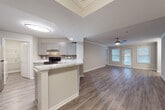 This single-floor residence presents a thoughtfully designed layout with a cohesive, neutral color palette and modern finishes throughout. The open-concept living and dining area is spacious and airy, highlighted by wood-style luxury vinyl flooring, crown molding, and a ceiling fan. Large windows fitted with slatted blinds allow generous natural light to fill the space, while a glass-paned door provides access to an outdoor area. The entryway is welcoming, featuring a classic paneled front door that opens directly into the expansive common living space.

The kitchen is well-appointed and efficiently arranged, featuring gray shaker-style cabinetry, marble-look quartz countertops, a tiled backsplash, and stainless steel appliances including a range and refrigerator. A peninsula with seating overhang connects the kitchen to the living area, reinforcing the open flow. A separate laundry or utility room is accessible directly from the kitchen.

The bedroom offers plush carpeted flooring and ample wall space, providing a quiet retreat. Two bathrooms are present — one featuring a wide vanity with marble-look countertops, a large mirror, and a tub-shower combination with accessibility grab bars, and a second with similar finishes and a tub-shower. Both bathrooms maintain the light, neutral aesthetic consistent throughout the home.