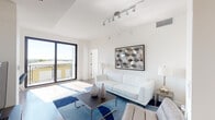 Located at 3180 SW 22nd St in Miami's vibrant Coral Way neighborhood, this modern single-floor residence showcases a clean, contemporary design throughout. The bright living area is anchored by large sliding glass doors that open to a private balcony, flooding the space with natural light and offering open outdoor views. Track lighting, crisp white walls, and light wood-style flooring create a cohesive, airy aesthetic. A bold blue area rug and geometric wall art add character to the living space.

The kitchen features a sleek two-tone design with white upper cabinetry, charcoal lower cabinets, white countertops, and a full suite of stainless steel appliances, including a French door refrigerator, microwave, and dishwasher. Light wood flooring extends throughout the main living areas.

The bedrooms are bright and well-proportioned, bathed in natural light from floor-to-ceiling windows. The primary bedroom includes a dedicated walk-in closet. A secondary bedroom offers balcony access and flexible use as a sitting room or home office. Both bathrooms are finished with wood-look tile surrounds, large-format floor tiles, and modern gray vanities with white countertops. A hallway with louvered closet doors and a utility panel connects the private areas of the residence efficiently.