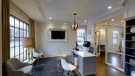 This two-floor property combines polished interior workspaces with thoughtfully designed outdoor amenities. The interior office space is elegantly appointed, featuring crown molding, a tray ceiling with recessed lighting, and warm hardwood flooring. A statement globe pendant light anchors the room, which is outfitted with a large L-shaped desk, ergonomic seating, and a wall-mounted flat-screen television framed in a decorative surround. Natural light filters through a window, while an adjacent room with patterned wallcovering adds visual depth to the layout.

Outside, the property offers a generously sized swimming pool with tiled edges and a surrounding concrete sundeck lined with blue lounge chairs, ideal for relaxing under open skies. A dedicated outdoor dining area features a rustic wood farmhouse table with seating for several guests, positioned alongside a living plant wall that adds a lush, natural accent. A poolside utility structure provides additional storage and functional support for the outdoor space.

The grounds are enclosed by a sturdy wrought iron and brick perimeter fence, offering privacy and security. Mature trees provide natural shade throughout the exterior areas, and a well-maintained lawn adds greenery to the setting. Neighboring multi-story residential buildings frame the backdrop, situating this property within an established community environment.