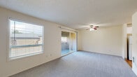 This compact single-floor unit offers a practical and efficient layout across two bedrooms, one bathroom, a kitchen, and an entrance. The living area is carpeted and filled with natural light from a large side window and sliding glass door, which opens to an outdoor space and provides views of the surrounding area. A ceiling fan with an integrated light fixture serves as a functional centerpiece overhead, complemented by a textured ceiling throughout.

The primary bedroom is a well-proportioned room featuring carpet flooring, a built-in closet with sliding doors, and a window that allows for additional natural light. The second bedroom is similarly carpeted and includes a window overlooking the outdoors, making it a bright and usable space.

The kitchen is efficiently designed with white cabinetry, both upper and lower storage, a stainless steel sink, laminate countertops, and hardwood-style flooring. An adjacent storage closet with shelving adds practical utility. The bathroom features a full tub and shower combination with floor-to-ceiling beige square tile surround and chrome fixtures, providing a clean and functional space. Overall, the unit offers a straightforward, functional design suited for efficient everyday living.