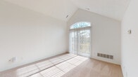This single-floor residence is defined by its striking architectural character, most notably the vaulted ceilings that rise dramatically in the main living area, creating an open and airy atmosphere. A large arched transom window crowns a set of sliding glass doors fitted with vertical blinds, allowing abundant natural light to flood the space and illuminate the plush, neutral-toned carpeting below. The generous scale of this room makes it well-suited as a primary living or sitting area, and a door leads conveniently to an adjoining space.

Additional carpeted rooms offer comfortable proportions and bright outlooks, each with windows dressed in vertical blinds that provide outdoor views and natural light. The white walls and clean finishes throughout maintain a consistent, neutral palette.

The kitchen is efficiently laid out with white cabinetry extending to the ceiling, a full suite of white appliances including a range and refrigerator, and light tile flooring. A dedicated laundry area with a full-size washer and dryer sits directly off the kitchen, adding practical convenience.

Two bathrooms complete the layout. The primary bathroom features a wide vanity with an extended countertop, a large mirror, and mosaic tile flooring. The second bathroom offers a walk-in glass-enclosed shower, toilet, and matching tile flooring, providing a compact yet fully functional space.