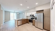 Located in Phoenix, AZ, this well-designed 2-bedroom, 1-bathroom residence offers a thoughtful layout across a single floor. The open-concept kitchen and living area serves as the heart of the home, featuring a large central island with a quartz countertop, undermount sink, and pendant lighting overhead. The kitchen is equipped with a full suite of stainless steel appliances—including a French door refrigerator with ice maker, electric range, built-in microwave, and dishwasher—complemented by two-tone cabinetry with white upper cabinets and warm wood-toned lower cabinets. Light wood-look flooring runs throughout, lending a clean, cohesive feel. The primary bedroom is generously sized and includes a ceiling fan and sliding glass door that opens to an outdoor view of lush greenery. A dedicated closet with built-in shelving and hanging rods provides organized storage. The second bedroom also features a ceiling fan and a closet with shelving. The bathroom is finished with a wood-toned vanity, quartz countertop, and a glass-enclosed walk-in shower with tile surround. Neutral-toned walls and recessed lighting throughout create a bright, modern ambiance well-suited to the Arizona lifestyle.
