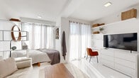 Located at 2936 Summit St in Kansas City's vibrant 64108 zip code, this single-floor studio unit presents a thoughtfully arranged open-concept layout bathed in natural light. The main living area seamlessly integrates sleeping, lounging, and working zones, separated by an open white shelving unit that adds visual structure without sacrificing the sense of openness. Large windows dressed in sheer white curtains allow abundant daylight to fill the space, enhancing the bright, airy atmosphere created by the predominantly white interior palette and light-toned flooring.

The living area accommodates a tufted cream sofa, a mid-century style wood coffee table, and a dedicated workspace with a desk and chair, offering practical versatility. The kitchen is efficiently designed with dark espresso cabinetry, stainless steel countertops, a stainless sink, built-in microwave, compact refrigerator, and a cooktop — providing all essential cooking amenities within a compact footprint.

The bathroom continues the clean aesthetic with marble-effect wall tiling, a shower with curtain, toilet, and a vanity with mirror and storage. Throughout the unit, the consistent white tones, recessed lighting, and streamlined furnishings create a cohesive, modern, and functional living environment.