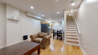 This two-floor residential space is designed for comfortable, functional living, with light hardwood flooring running consistently throughout to create a cohesive and warm aesthetic. The main level opens into a combined living, dining, and kitchen area. The living space accommodates a seating area and coffee table, with recessed lighting overhead and a window that allows natural light to filter in. The dining area sits adjacent, centered around a dark wood table and chairs. The kitchen is well-equipped with warm maple cabinetry, granite-style countertops, stainless steel appliances including a range, dishwasher, and a French door refrigerator with an ice dispenser, plus an over-range microwave. A staircase with light wood treads and white railings connects the floors. The bedrooms are bright and neutrally finished, with recessed lighting, closet storage, and windows offering natural light — one bedroom notably features a dual-window layout. The bathrooms are cleanly finished with light tile flooring, wood-toned vanities, oval mirrors, and baseboard heating. The overall layout, as seen in the 3D floorplan, is elongated and well-organized, providing clearly defined spaces across both levels.