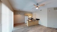This single-floor space showcases an open-concept layout that seamlessly connects the kitchen and living areas. The kitchen is equipped with light maple cabinetry, a white refrigerator, and a range with an overhead exhaust hood. A dark-countertop peninsula with an integrated sink and breakfast bar overhang serves as both a functional workspace and a casual dining area, accommodating bar-style seating. The open flow between the kitchen and living space creates a welcoming, practical environment well-suited for everyday living and entertaining.

Underfoot, light-toned laminate flooring runs throughout, contributing to a clean and cohesive aesthetic. Overhead, a ceiling fan with an integrated light fixture provides both airflow and ambient lighting to the main living area, while a pendant light adds a focused accent above the dining zone. Recessed lighting supplements the illumination in the kitchen area. The textured ceiling adds subtle visual interest. Neutral wall tones in warm beige and gray keep the space feeling bright and versatile, offering a blank canvas for personalization.