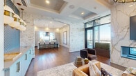 This elegantly designed single-floor space offers a generously sized open-plan layout that seamlessly integrates the living, dining, and kitchen areas into a cohesive, upscale environment. Rich hardwood flooring runs throughout, providing a warm foundation that complements the refined finishes found across each zone.

The living area is anchored by a striking marble-clad fireplace wall and a coffered ceiling fitted with a statement chandelier. Floor-to-ceiling windows and glass doors flood the space with natural light while framing panoramic city skyline views, creating an impressive indoor-outdoor connection with access to an outdoor terrace.

A dramatic whitewashed brick archway transitions into the kitchen, which features a large waterfall-edge island with white upholstered barstools on brass frames, complemented by sleek cabinetry and pendant lighting in a globe design with gold accents.

The dining area is positioned to maximize the sweeping city views through expansive floor-to-ceiling glazing, topped by an elegant linear chandelier. A separate conference-style dining room offers a long hardwood table, bold patterned wallcovering, built-in cabinetry, a wall-mounted display, and its own statement chandelier — ideal for formal gatherings or professional use.
