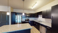 This single-floor unit in Wyoming, Michigan offers a thoughtfully designed layout that balances style and functionality. The kitchen is a standout feature, boasting dark espresso cabinetry, granite countertops, a central island, and a full suite of stainless steel appliances including a refrigerator, range, microwave, and dishwasher. A built-in wine rack and track lighting add refined touches, while light hardwood-style flooring ties the space together seamlessly.

The living area is generously proportioned, featuring a ceiling fan, hardwood-style flooring, and direct access to an outdoor balcony through a glass door, allowing for ample natural light. The bedrooms are carpeted for comfort and equipped with ceiling fans; large windows in each room frame pleasant outdoor views of surrounding greenery.

The bathrooms are finished consistently with the kitchen's aesthetic, showcasing granite-topped dark vanities, large mirrors with overhead lighting, and a full tub-shower combination. Light wood-style flooring continues through the bathrooms, complementing the neutral wall tones throughout the unit. Overall, the space presents a cohesive, modern design with quality finishes at every turn.