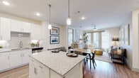 This single-floor residence offers a thoughtfully designed open-concept layout that seamlessly connects the kitchen, dining, and living areas. The kitchen is a standout feature, outfitted with crisp white cabinetry, granite countertops, a large center island with pendant lighting, a subway tile backsplash, and a full suite of stainless steel appliances, including a range, microwave, dishwasher, and refrigerator. Wood-look flooring runs throughout the main living areas, adding warmth and continuity to the space.

The open living and dining area is bright and airy, benefiting from large windows and a glass patio door that invite abundant natural light and provide access to the outdoors. A ceiling fan completes the comfortable atmosphere of the living space.

The bedroom is a serene retreat, featuring plush carpeting, a generously sized window with garden views, and a ceiling fan. It connects directly to a private en-suite bathroom appointed with a granite-topped vanity, a glass-enclosed shower, wood-look flooring, and a spacious walk-in closet with multi-level shelving and hanging rods. Additional storage is provided by a dedicated utility closet near the kitchen. The overall palette of neutral tones and modern finishes creates a clean, cohesive aesthetic throughout.
