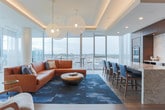 Located at 4000 Hillsboro Pike in Nashville's Green Hills neighborhood, this elegantly designed single-floor space offers a seamless blend of modern aesthetics and functional sophistication. Floor-to-ceiling glass walls flood the interior with natural light while framing breathtaking panoramic views of the Nashville cityscape and surrounding lush greenery.

The open-concept layout connects distinct living and entertaining zones with effortless flow. A spacious lounge area features warm leather seating, layered area rugs, and sculptural pendant lighting, with direct access to an outdoor terrace equipped with seating—ideal for enjoying the elevated views.

The gourmet kitchen is a standout feature, showcasing rich dark wood cabinetry, stainless steel appliances including a double wall oven and French door refrigerator, and a striking marble-topped island with blue upholstered bar seating. A textured stone backsplash anchors an integrated media display, adding a dynamic focal point to the culinary space.

A dedicated dining area positioned against the expansive glass walls offers an intimate setting with unobstructed views. Tray ceilings with recessed warm lighting add architectural depth throughout, while wide-plank hardwood and large-format tile flooring ground the space in refined, contemporary style. The overall ambiance is polished, airy, and thoughtfully curated.