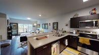 This single-floor residence is thoughtfully designed with a modern aesthetic, combining functionality and comfort across its well-defined living spaces. Rich, dark hardwood-style flooring flows consistently throughout, anchoring each room with a cohesive, contemporary feel.

The open-concept kitchen is equipped with dark espresso cabinetry, light countertops, and a full suite of stainless steel appliances, including a refrigerator, electric range, built-in microwave, and dishwasher. The U-shaped layout provides generous counter space, and the kitchen opens seamlessly into the living area, making it ideal for entertaining.

The living room is bright and welcoming, featuring large windows that draw in natural light and offer views of surrounding greenery. A tiled fireplace serves as a focal point, while sliding glass doors lead to a private balcony furnished with outdoor seating—an appealing extension of the living space.

Two bedrooms offer comfortable retreats, each with dark-toned doors, hardwood-style flooring, and windows with outdoor views. One bedroom includes a built-in window seat, adding a functional and charming design detail.

The bathroom continues the modern theme with dark cabinetry, wood-look flooring, and clean neutral walls, completing this well-rounded residence.