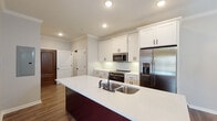 This single-story, 2-bedroom, 2-bathroom unit in Jonesboro, Arkansas offers a well-designed layout with contemporary finishes throughout. The kitchen serves as a central highlight, featuring crisp white shaker-style cabinetry with black hardware, a white quartz countertop island with a undermount double sink, a white subway tile backsplash, and a full suite of stainless steel appliances including a French door refrigerator, electric range, and built-in microwave. Crown molding and recessed lighting add a polished touch to the space, which opens to a combined living and dining area adorned with a chandelier and wall sconce lighting. Warm wood-look flooring runs consistently throughout the unit, enhancing the cohesive aesthetic. Both bedrooms are generously sized, offering natural light through blinded windows and ceiling fans for comfort. The primary bathroom includes an ADA-accessible tub/shower with grab bars and a white vanity with a framed mirror, while the second bathroom features a standard tub/shower combo with black fixture accents and matching vanity cabinetry. The open floor plan and neutral color palette create a bright, functional living environment.