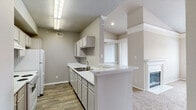 This single-floor residence offers a thoughtfully designed layout with a seamless connection between the kitchen and living areas. The kitchen is equipped with gray cabinetry, light quartz countertops, a double stainless steel sink with a brushed nickel faucet, and a peninsula that opens to the living space—ideal for entertaining. The living area features vaulted ceilings with elegant crown molding details and a fireplace framed by a classic white mantel, adding warmth and character. Wood-look flooring runs through the kitchen and utility areas, while plush carpet flows throughout the living spaces and bedrooms. The bedrooms are generously sized, each filled with natural light through large windows, including an arched window and a wide picture window with outdoor views. A ceiling fan provides comfort in one of the bedrooms. The primary bathroom includes a wide vanity with gray cabinetry, a large mirror, and wood-look flooring. A spacious walk-in closet with wire shelving offers ample storage. A dedicated laundry room houses the water heater and washer/dryer connections, with additional wire shelving overhead. Textured ceilings are featured throughout, and the neutral color palette creates a clean, cohesive atmosphere across the entire space.